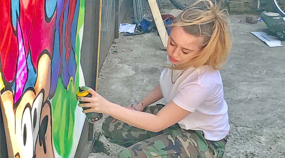 Teenage girl spray painting on a canvas.