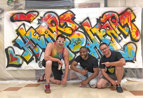 3 men posing front of graffiti canvas